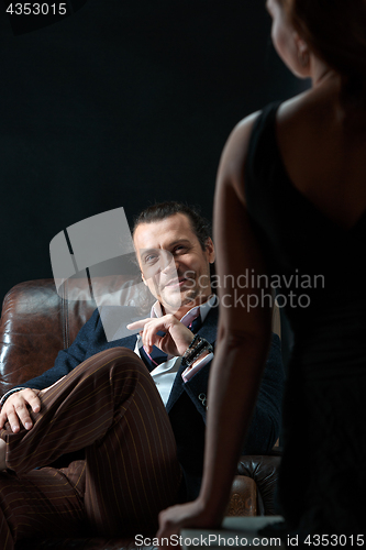 Image of The artist or mature man wearing suit in a classical retro fashion style. The woman standing near