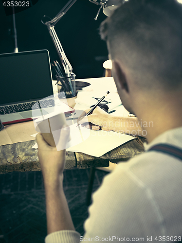 Image of Vintage hipster wooden desktop side view, male hands with cup and holding a pencil