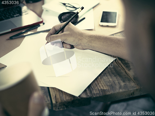 Image of Vintage hipster wooden desktop side view, male hands with cup and holding a pencil