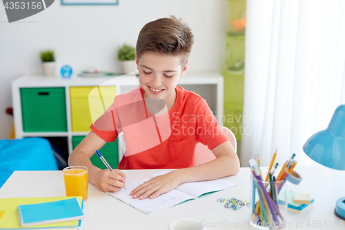 Image of happy student boy writing to notebook at home