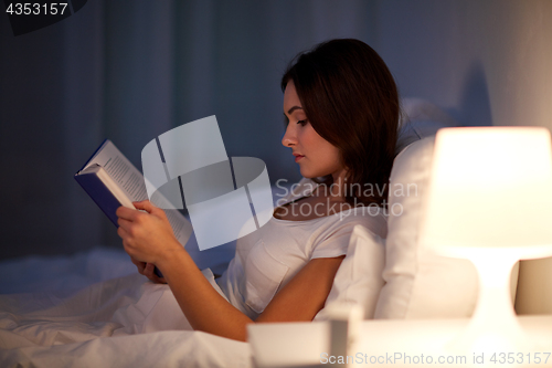 Image of young woman reading book in bed at night home