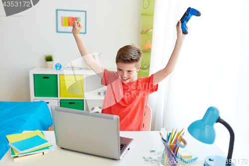 Image of boy with gamepad playing video game on laptop