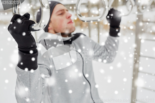 Image of young man exercising on horizontal bar in winter