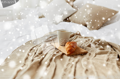 Image of coffee cup and croissant on plaid in bed at home