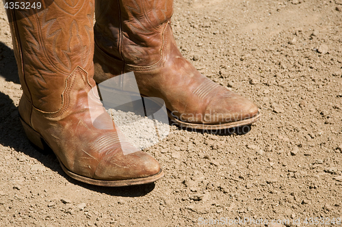 Image of Two dirty western cowboy boots standing on dirt ground