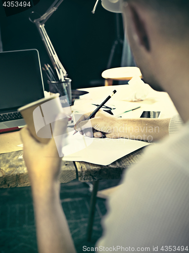 Image of Vintage hipster wooden desktop side view, male hands with cup and holding a pencil