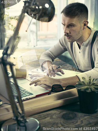 Image of Portrait of a bearded businessman who is checking details of his upcoming meeting in his notebook and typing.