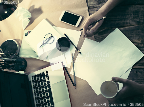 Image of Vintage hipster wooden desktop side view, male hands with cup and holding a pencil