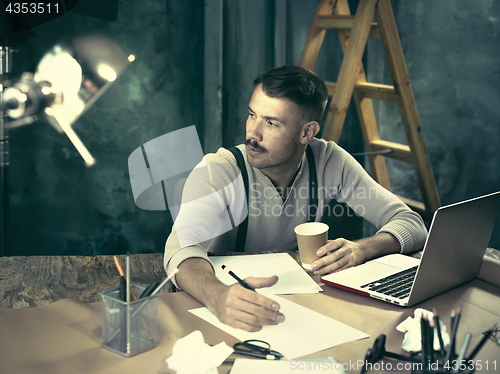 Image of Portrait of a bearded businessman who is checking details of his upcoming meeting in his notebook and typing.