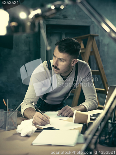 Image of Portrait of a bearded businessman who is checking details of his upcoming meeting in his notebook and typing.
