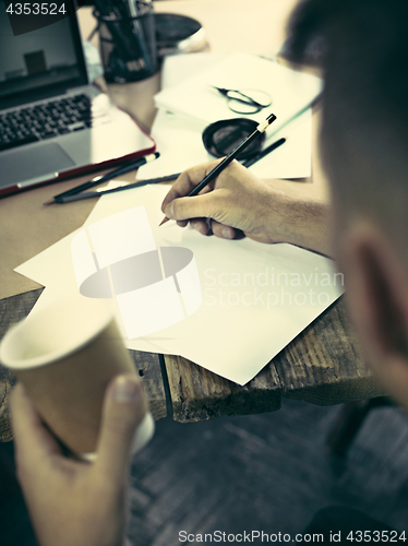 Image of Vintage hipster wooden desktop side view, male hands with cup and holding a pencil