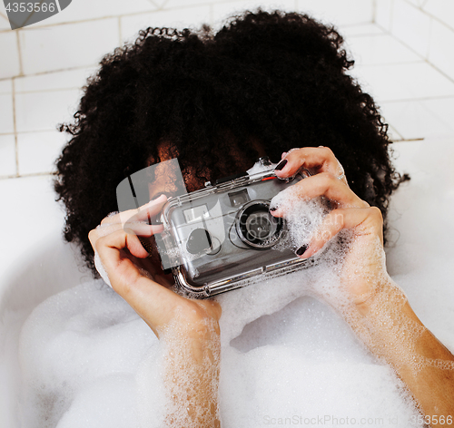 Image of young afro-american teen girl laying in bath with foam, wearing 