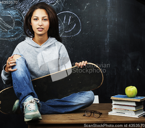 Image of young cute teenage girl in classroom at blackboard seating on table smiling, modern hipster concept