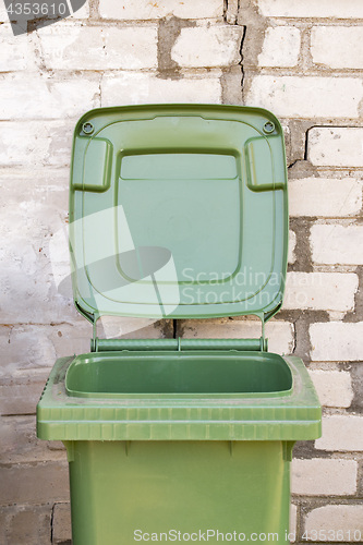 Image of Empty dirty green recycle bin near the brick wall