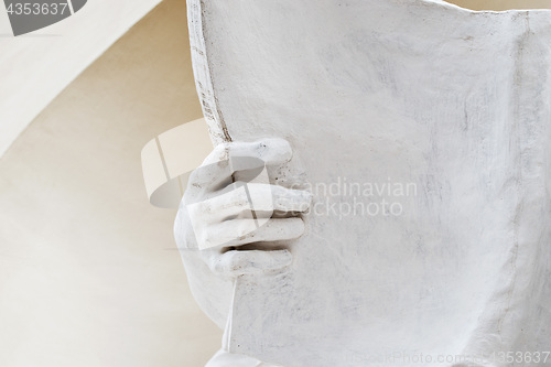 Image of stone statue detail of human hand holding book