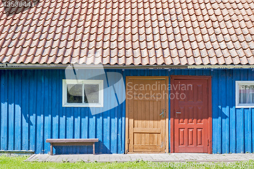 Image of House of blue wooden planks, red roof, two colorful doors and small windows