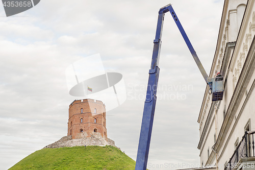 Image of Gediminas tower on green hill, construction worker fixing house facade