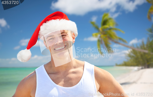 Image of happy young man in santa hat on beach at christmas