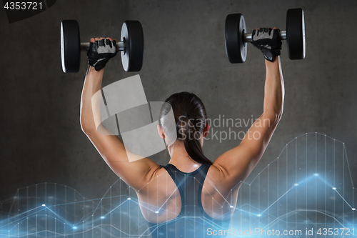 Image of young woman flexing muscles with dumbbells in gym