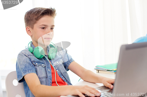 Image of happy boy with headphones typing on laptop at home