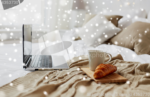 Image of laptop, coffee and croissant on bed at cozy home