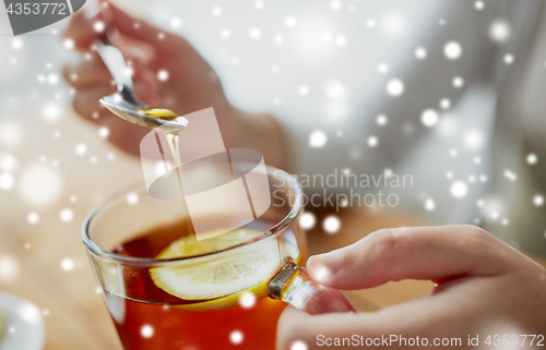 Image of close up of woman adding honey to tea with lemon