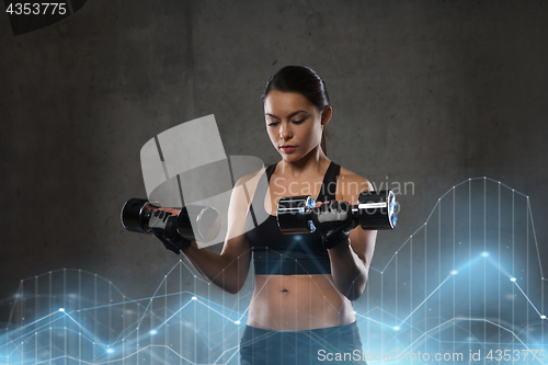 Image of young woman flexing muscles with dumbbells in gym