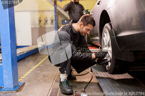 Image of auto mechanic with screwdriver changing car tire