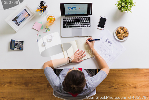 Image of woman with laptop writing to notebook at office