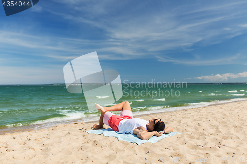 Image of happy smiling young man sunbathing on beach towel