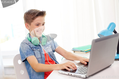 Image of happy boy with headphones typing on laptop at home