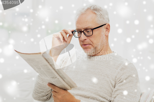 Image of senior man in glasses reading newspaper over snow