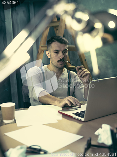 Image of Portrait of a bearded businessman who is checking details of his upcoming meeting in his notebook and typing.