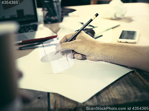Image of Vintage hipster wooden desktop side view, male hands with cup and holding a pencil
