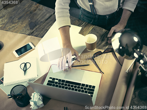 Image of Vintage hipster wooden desktop top view, male hands using a laptop and holding a pencil