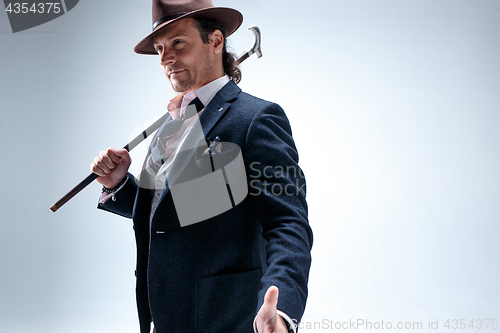 Image of The mature man in a suit and hat holding cane.