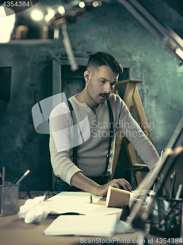 Image of Portrait of a bearded businessman who is checking details of his upcoming meeting in his notebook and typing.