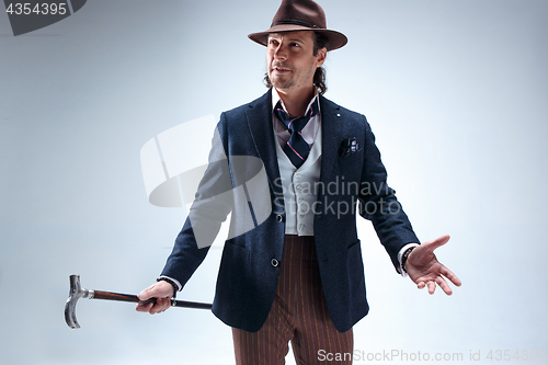 Image of The mature man in a suit and hat holding cane.