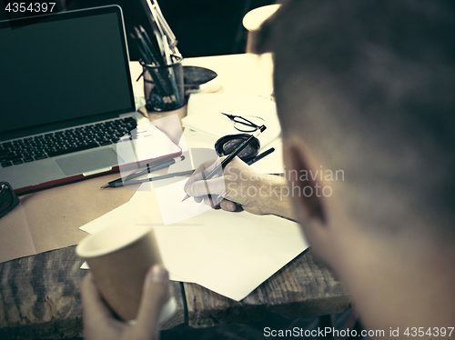 Image of Vintage hipster wooden desktop side view, male hands with cup and holding a pencil