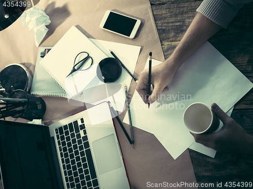Image of Vintage hipster wooden desktop side view, male hands with cup and holding a pencil