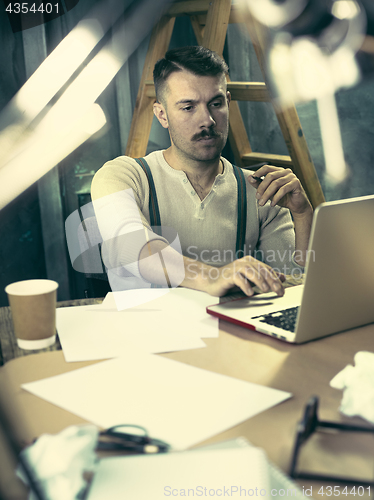 Image of Portrait of a bearded businessman who is checking details of his upcoming meeting in his notebook and typing.