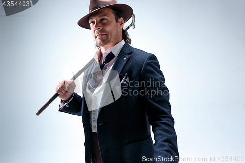 Image of The mature man in a suit and hat holding cane.