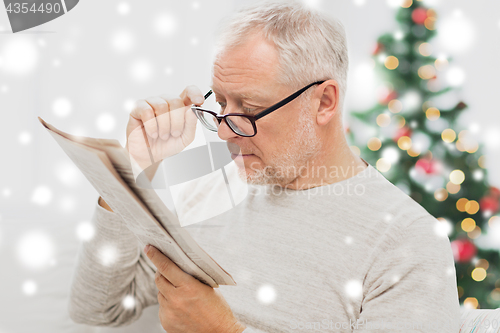 Image of senior man in glasses reading newspaper at home