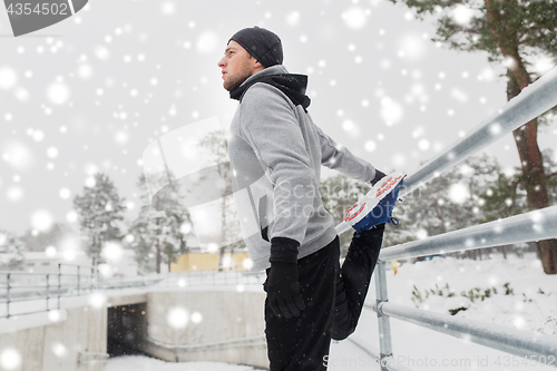 Image of sports man stretching leg at fence in winter