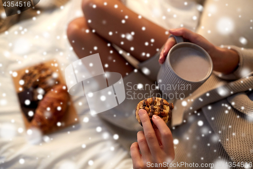 Image of close up of woman with cocoa cup and cookie in bed