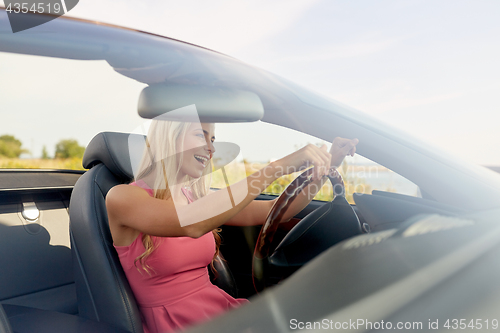 Image of happy young woman driving convertible car