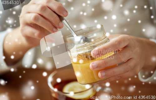 Image of close up of woman adding honey to tea with lemon