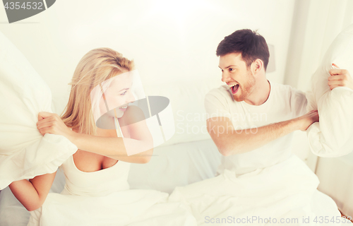 Image of happy couple having pillow fight in bed at home