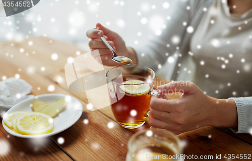 Image of close up of woman adding honey to tea with lemon