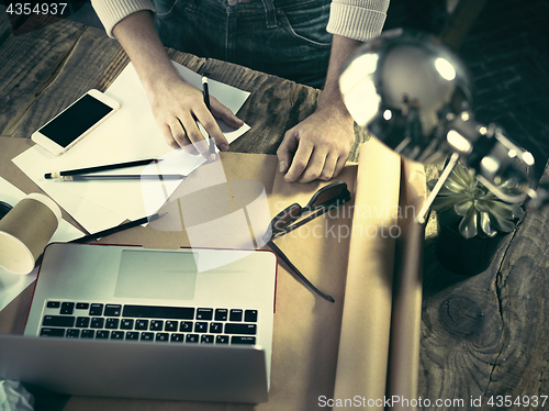 Image of Vintage hipster wooden desktop top view, male hands using a laptop and holding a pencil